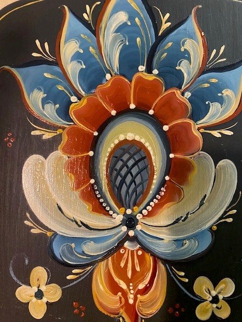 Close-up of a layered rosemaling flower in blue, rust, and cream on a black ground