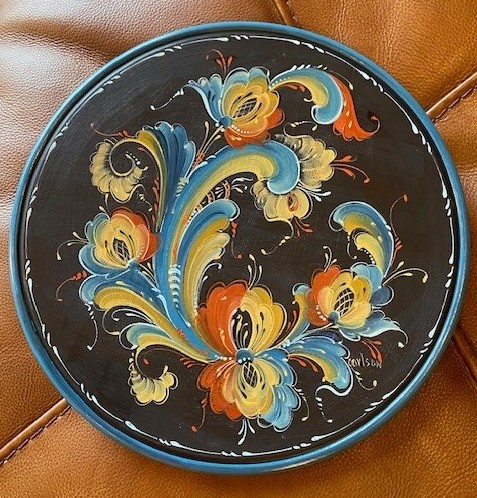 Round plate with flowing rosemaling scrollwork in blue, gold, and rust on a black ground
