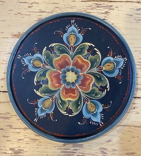 Round navy plate with a symmetrical rosemaling rosette in green, red, and blue