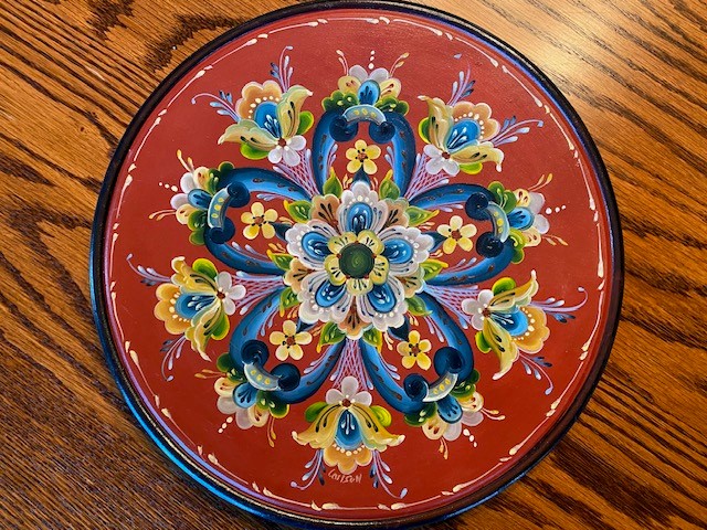 Round plate with a barn-red ground and a symmetrical rosette of blue, white, and gold flowers
