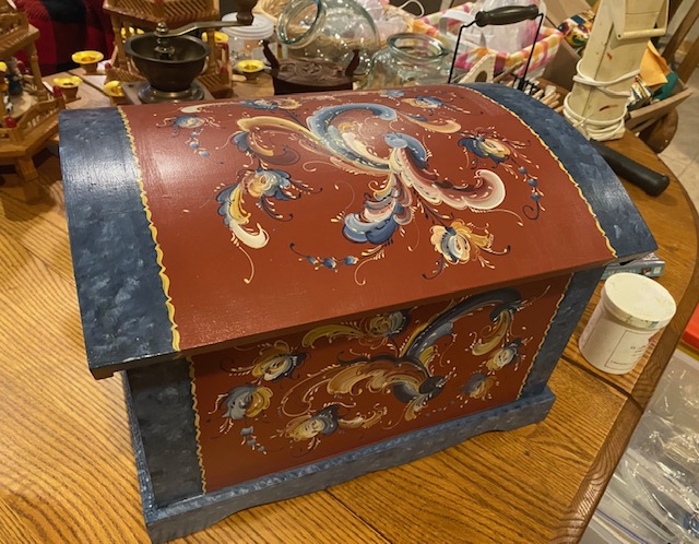 Dome-top trunk painted barn red with blue marbled trim and flowing rosemaling scrolls